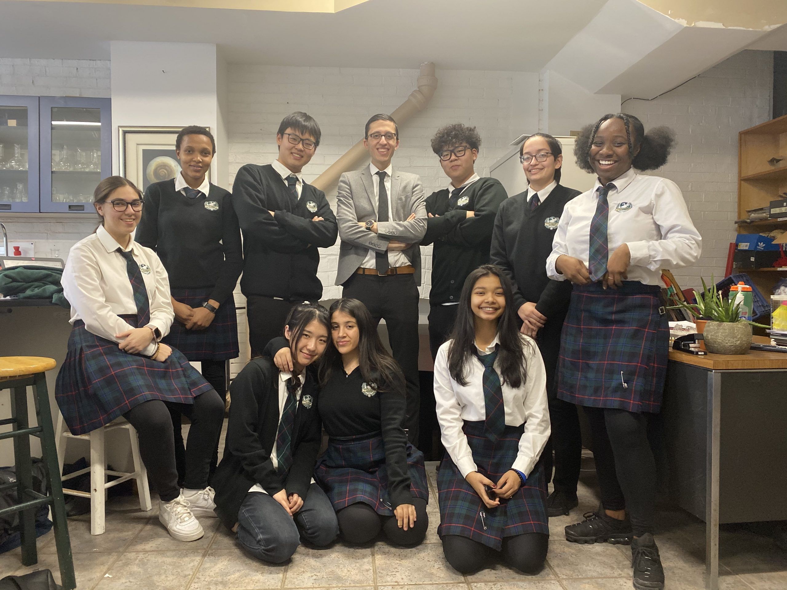 Mr. Saba Vejdani happily posing with students in his classroom looking professional